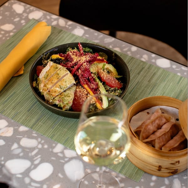 Grilled chicken salad with avocado, grapefruit, and beets, alongside dumplings and white wine.