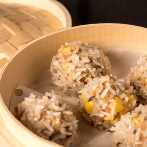 Steamed sticky rice balls with corn and other fillings in a bamboo steamer basket.