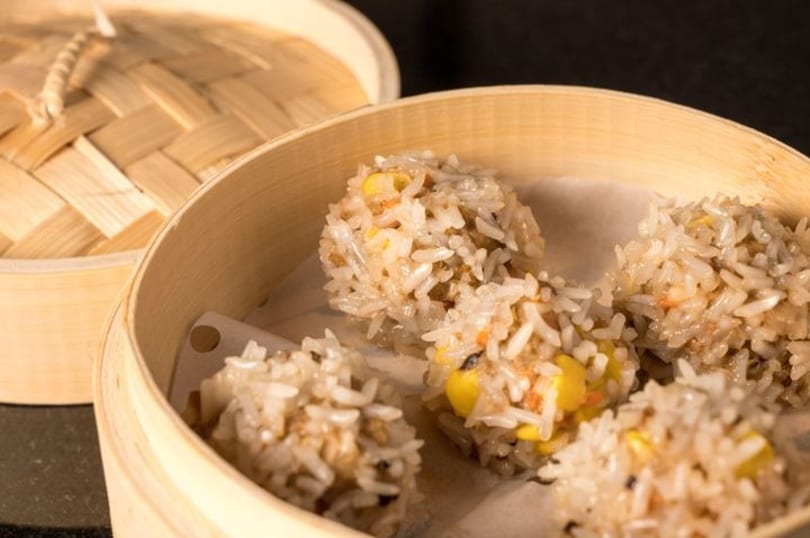 Steamed sticky rice balls with corn and other fillings in a bamboo steamer basket.