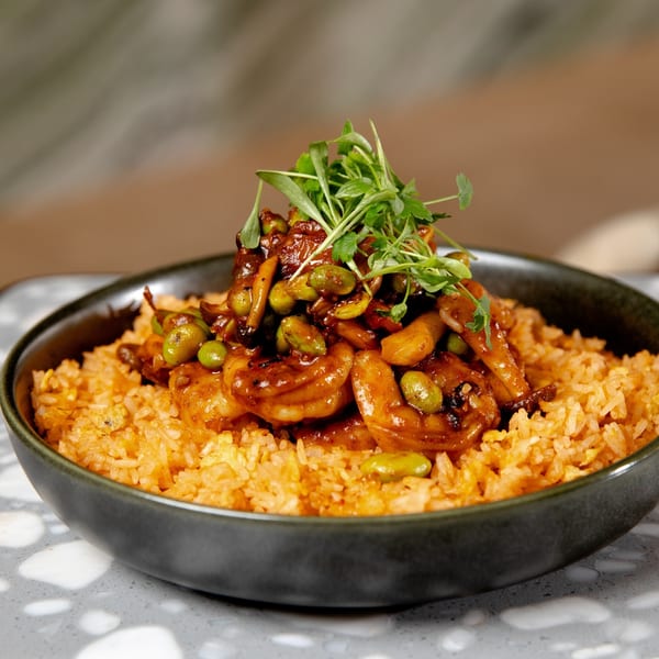 A dark bowl of orange fried rice topped with shrimp, edamame, and microgreens.