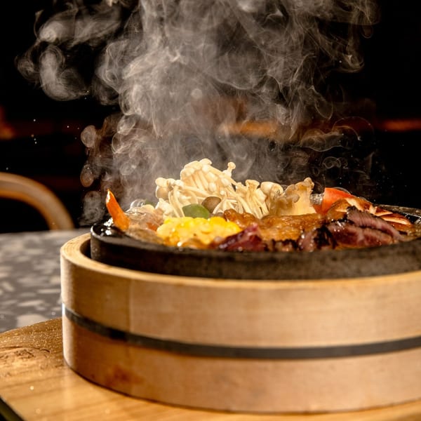 Steaming hot pot with mushrooms, meat, and vegetables in a dark, atmospheric setting.