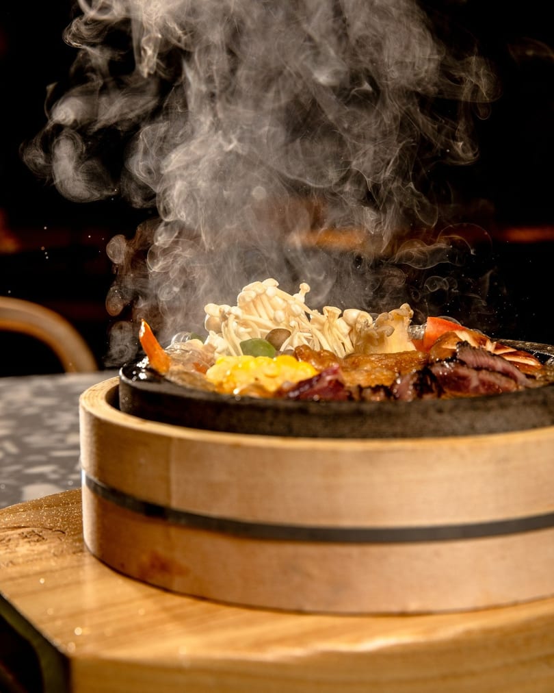 Steaming hot pot with mushrooms, meat, and vegetables in a dark, atmospheric setting.
