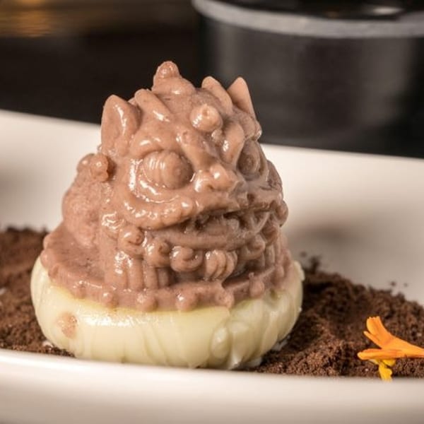 A dessert shaped like a mythical creature, with a brown top and white base, on chocolate crumbs.
