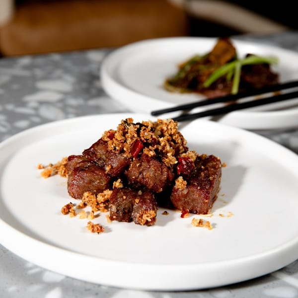 Close-up of diced beef with crispy garlic and chili flakes on a white plate.